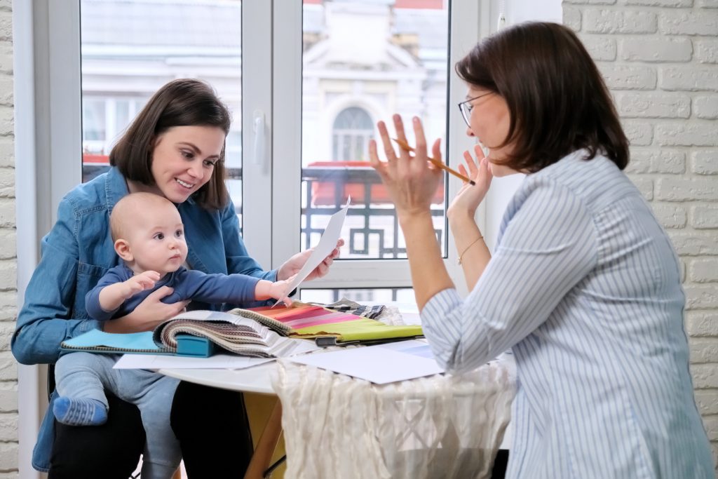 Women interior designer and client with baby choosing fabrics and materials